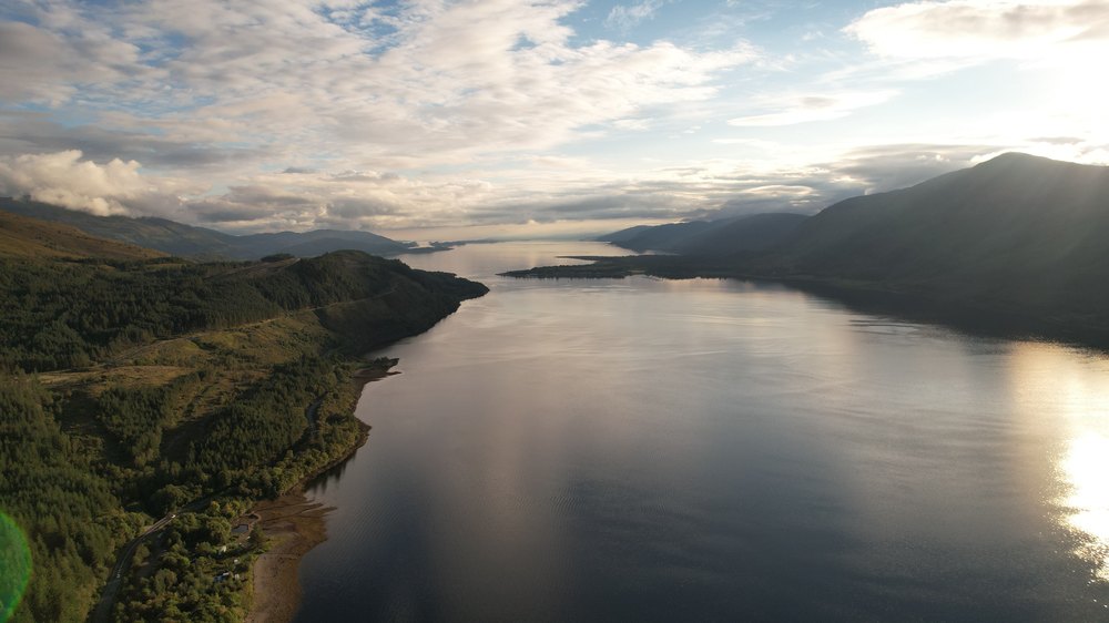 Długie jezioro Loch Ness między górami z lotu ptaka, światło słońca na wodzie