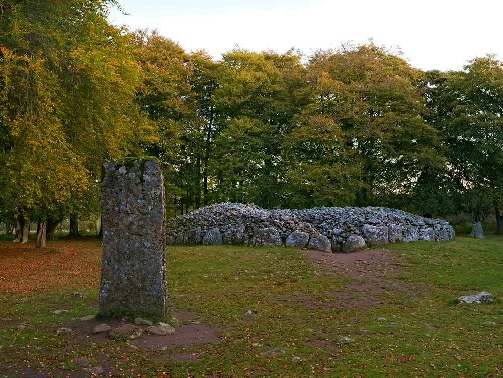 Pionowy głaz i kamienny kopiec grobowy Clava Cairns pod Inverness wśród drzew