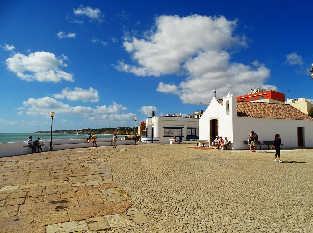 Biała kaplica na placu nad plażą w Armação de Pêra, wyłożonym kamienną kostką