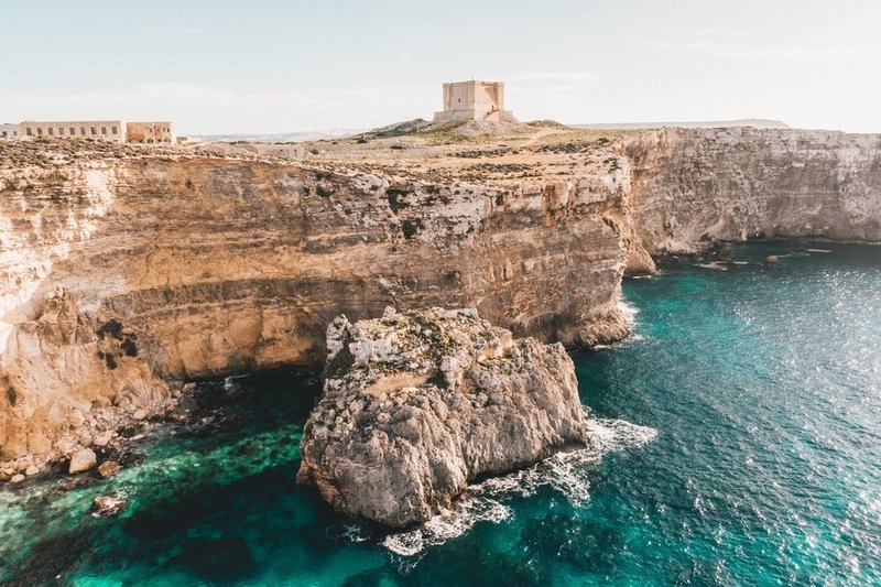 Wapienne klify i turkusowa woda Crystal Lagoon na Comino, w tle wieża Santa Marija