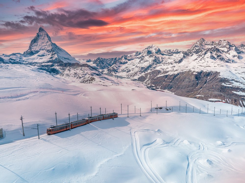Czerwony pociąg kolei zębatej na Gornergrat w śniegu, w tle Matterhorn o zachodzie