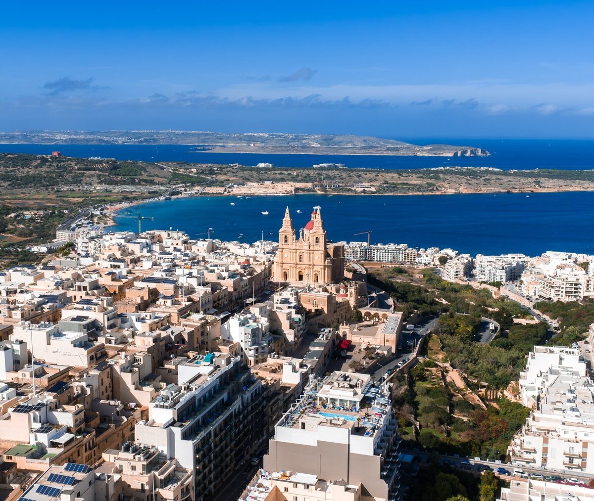 Mellieħa z lotu ptaka, kościół parafialny nad zabudową, zatoka, a na horyzoncie Comino i Gozo