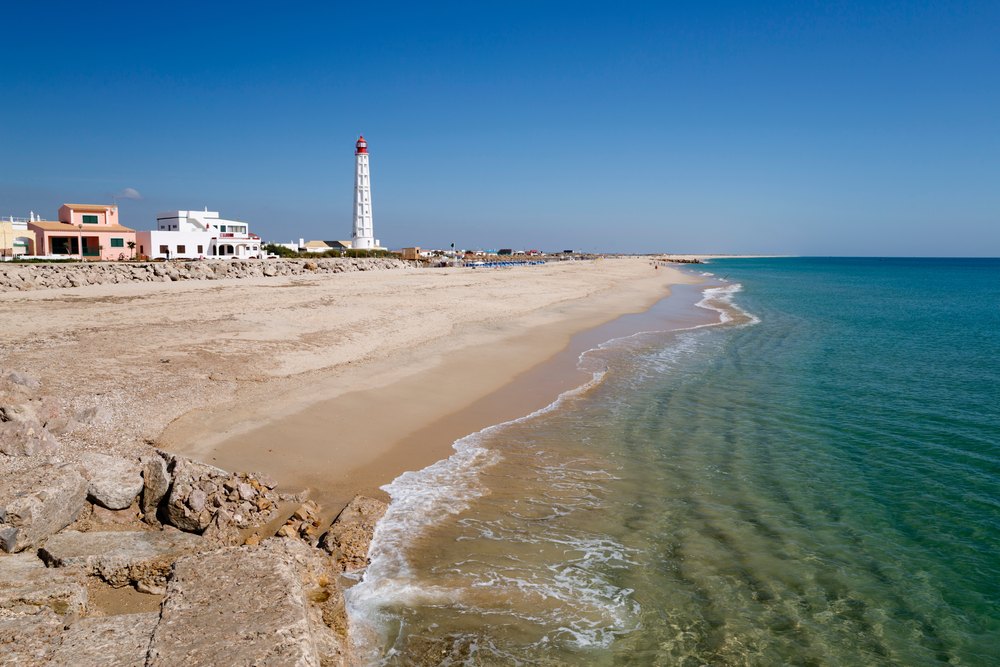 Plaża Farol na wyspie Culatra z latarnią morską i niskimi domami nad turkusową wodą