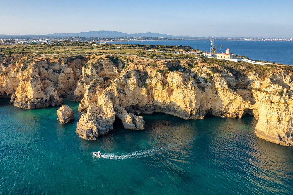 Latarnia morska na cyplu Ponta da Piedade nad klifami i łódź płynąca pod skały