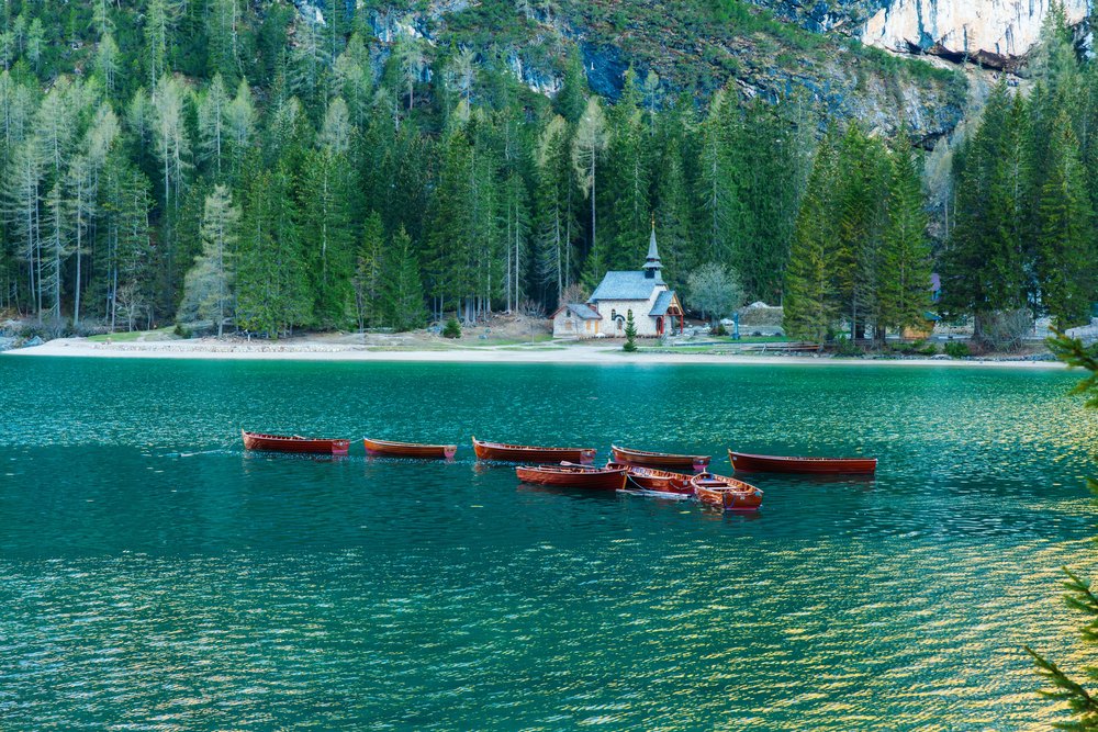 Drewniane łodzie wiosłowe na turkusowym Lago di Braies, na brzegu mała kaplica w lesie