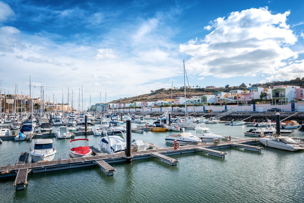 Jachty i łodzie przy pomostach Mariny de Albufeira, nad nią kolorowe domy na zboczu