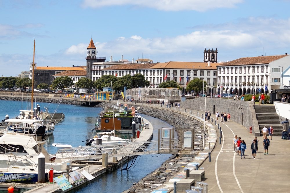 Marina w Ponta Delgadzie z jachtami przy pomostach i promenadą, w tle białe budynki z wieżami