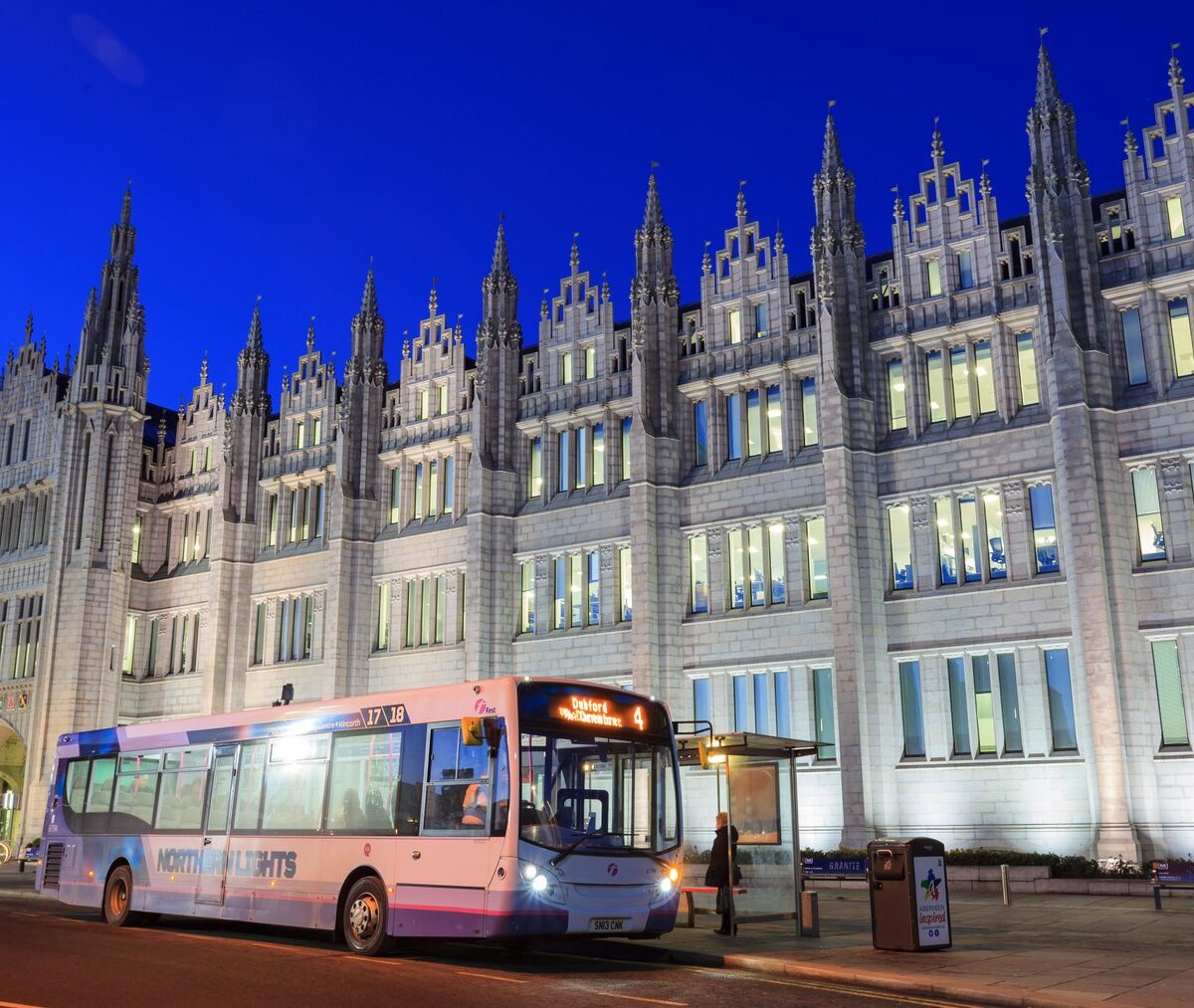 Podświetlona granitowa fasada Marischal College w Aberdeen wieczorem, przed nią autobus