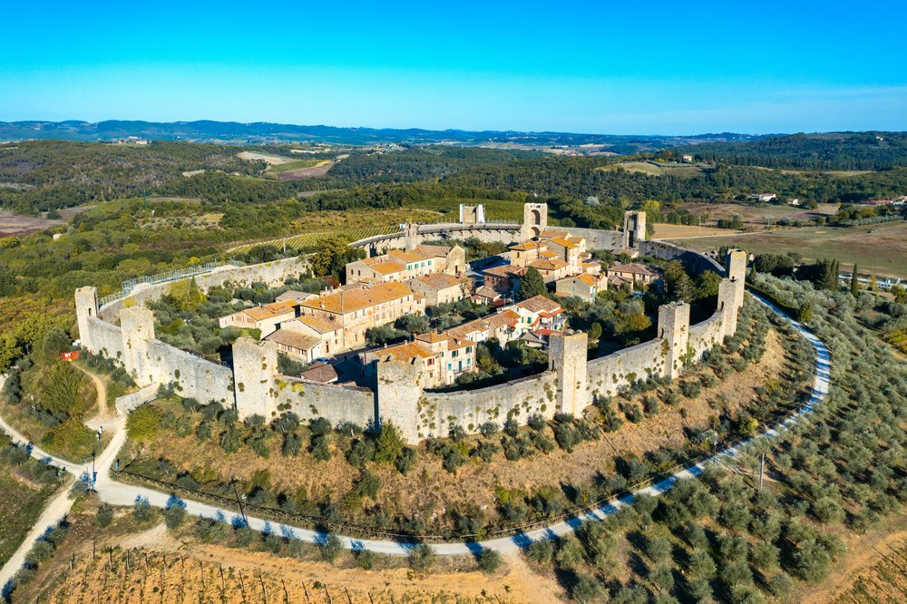Monteriggioni z lotu ptaka: owalny pierścień murów z basztami wokół wsi na wzgórzu wśród oliwek