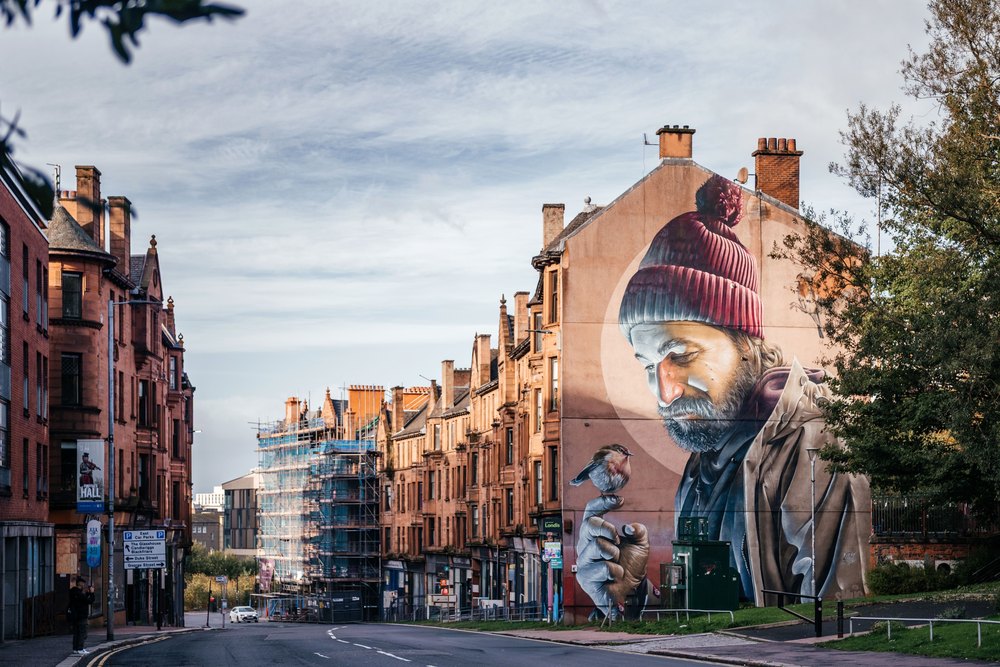 Mural ze świętym Mungo z ptakiem na dłoni na szczycie kamienicy przy ulicy w Glasgow