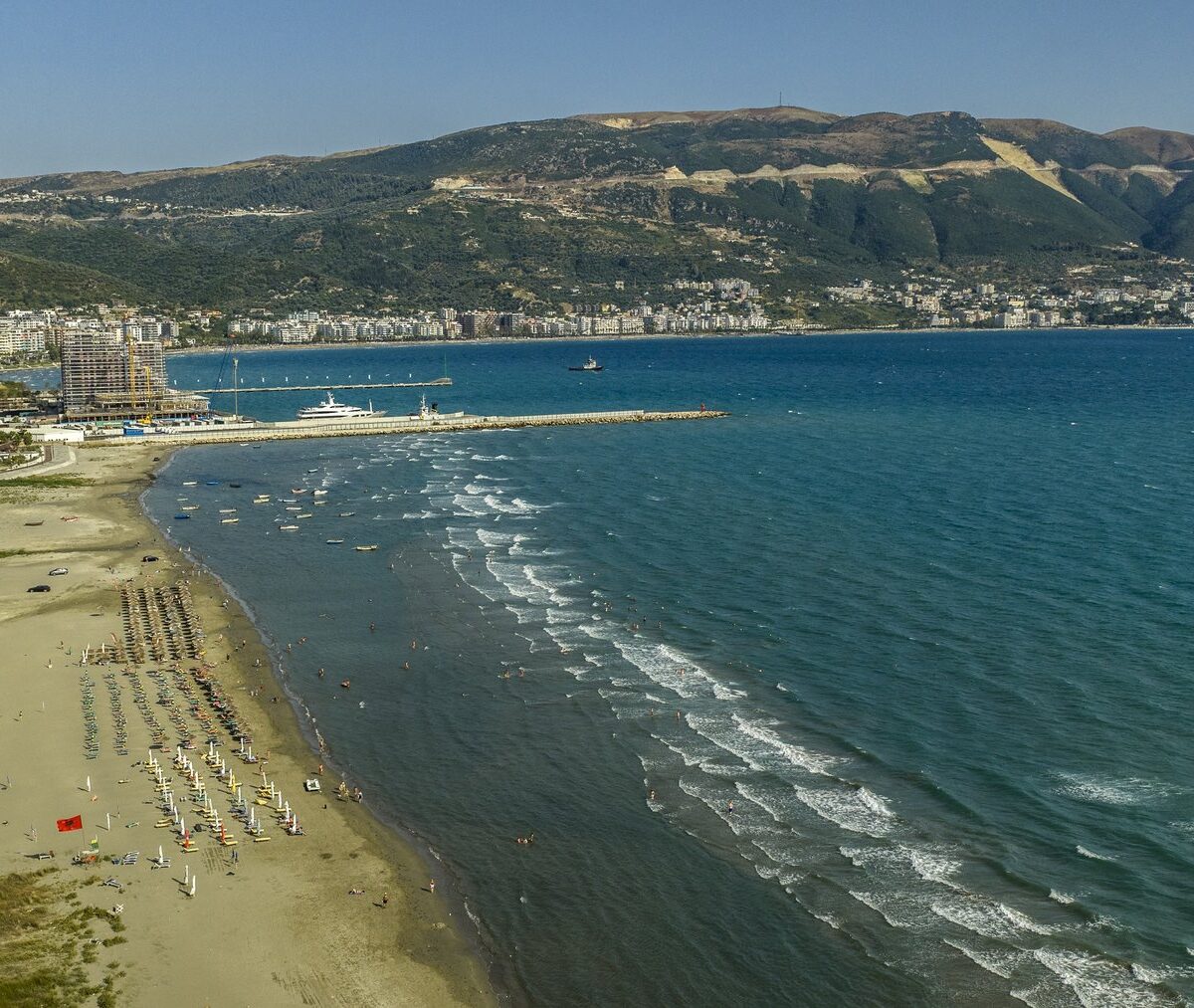 Piaszczysta plaża z parasolami i nabrzeże Wlory nad zatoką z lotu ptaka
