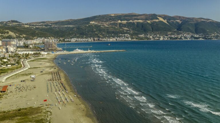Piaszczysta plaża z parasolami i nabrzeże Wlory nad zatoką z lotu ptaka