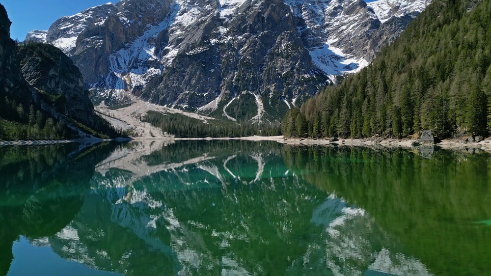 Ośnieżone szczyty i zielone zbocza odbite w spokojnej tafli Lago di Braies