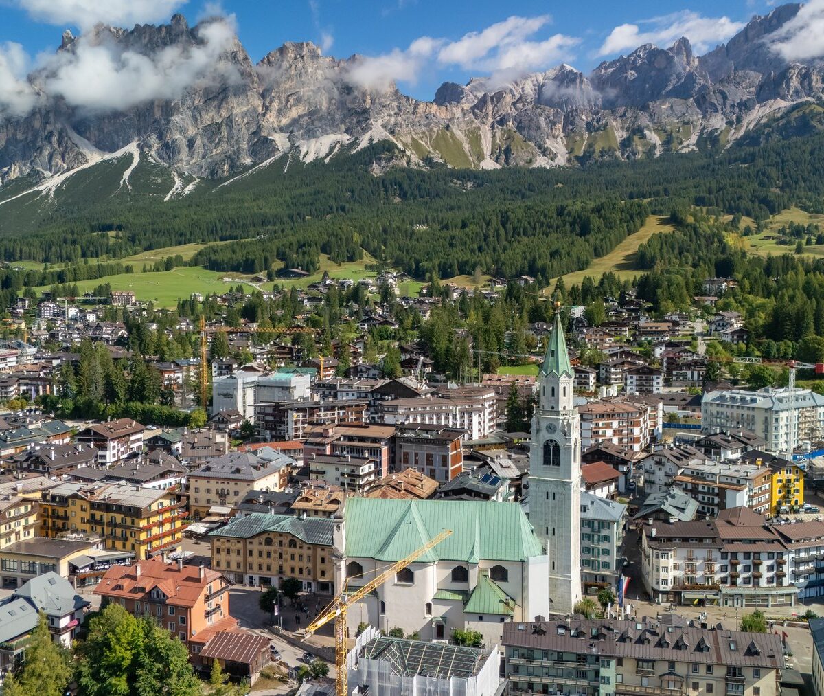 Cortina d'Ampezzo z lotu ptaka, bazylika z dzwonnicą w centrum miasta, nad nim skalne grzbiety Dolomitów