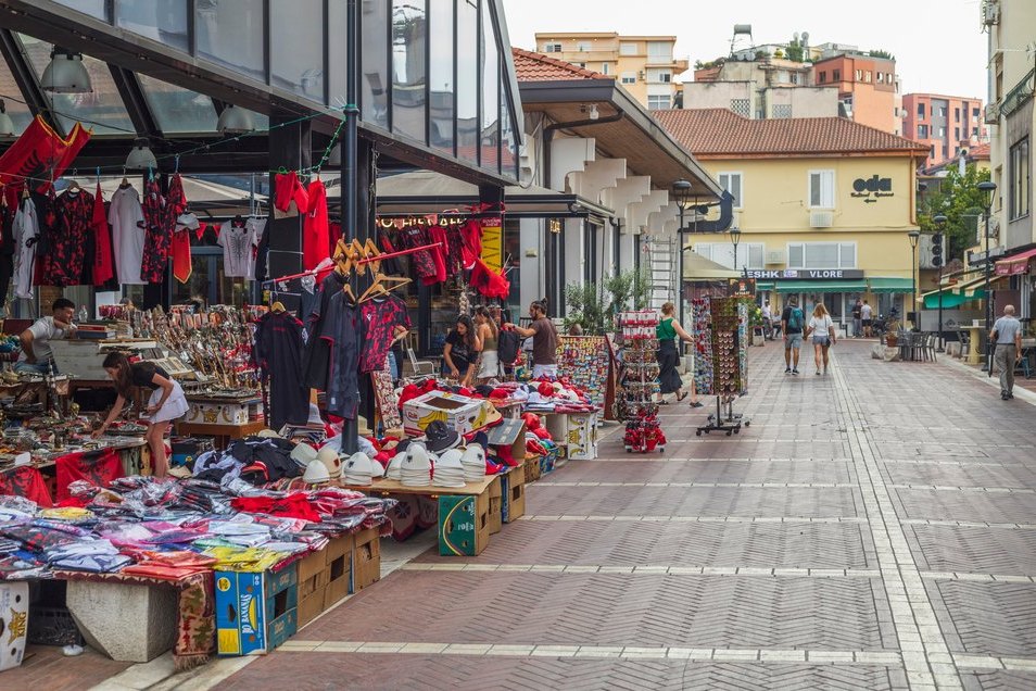 Stragany z koszulkami i pamiątkami przed halą targową ze szklanym dachem w Tiranie