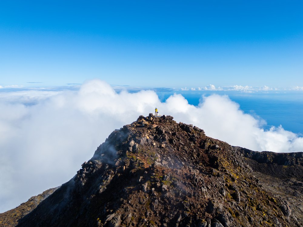 Turysta na szczycie Piquinho, najwyższym punkcie Pico, nad morzem chmur i oceanem