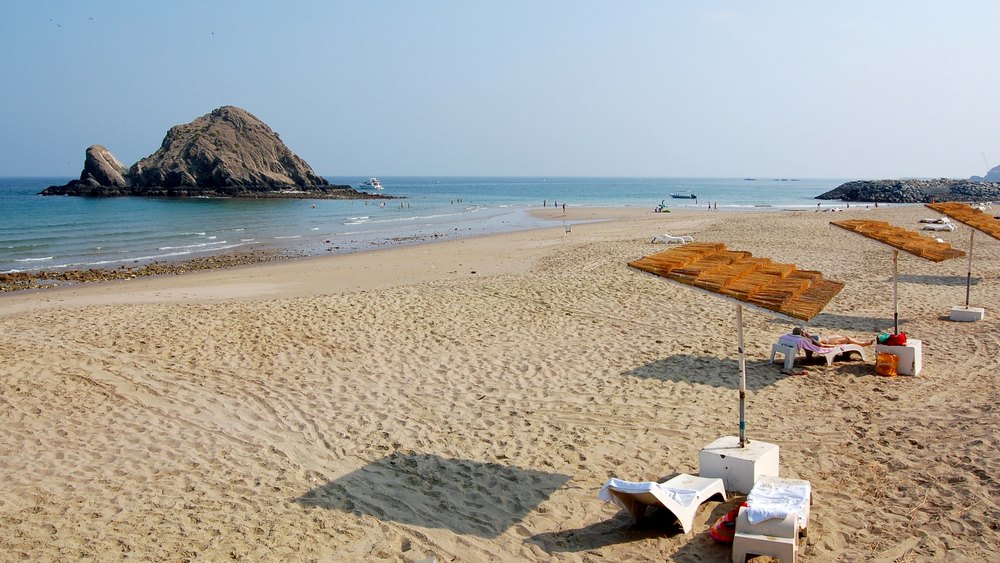 Piaszczysta plaża Al Aqah z parasolami, w tle skała Snoopy Island
