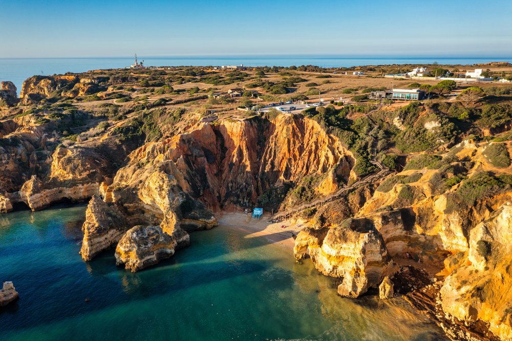 Zatoczka Praia do Camilo pod rzeźbionymi klifami, z drewnianymi schodami na zboczu