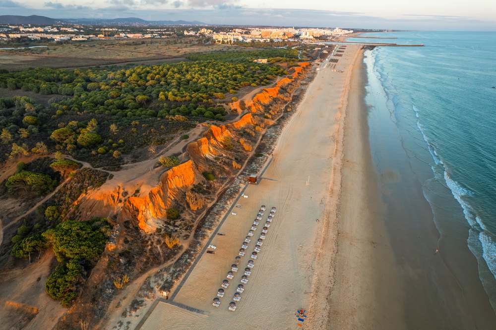 Praia da Falésia pod czerwonymi klifami i sosnami, długi pas piasku z lotu ptaka