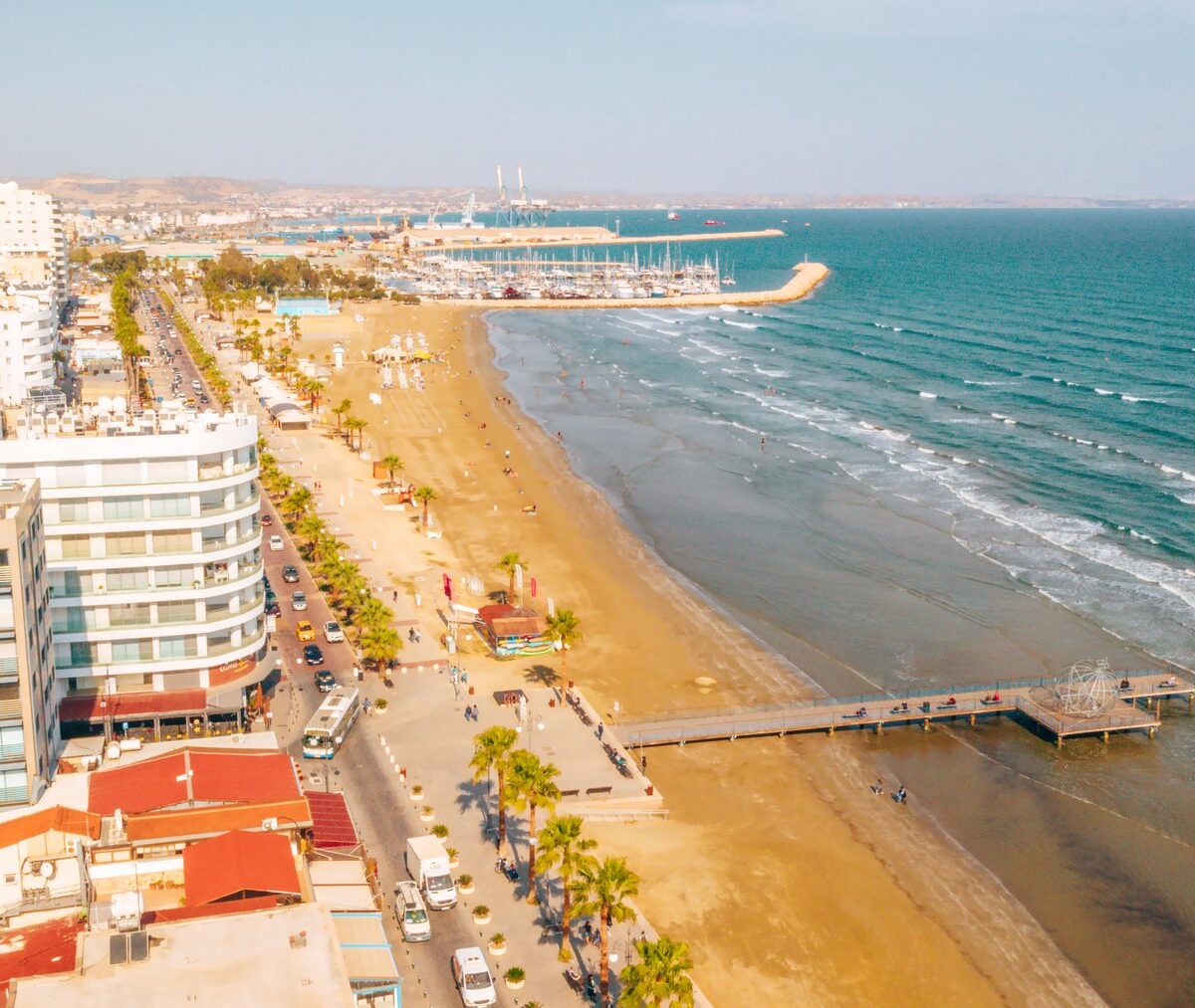 Plaża Finikoudes w Larnace z lotu ptaka, pomost, palmy i hotele wzdłuż nadmorskiej ulicy