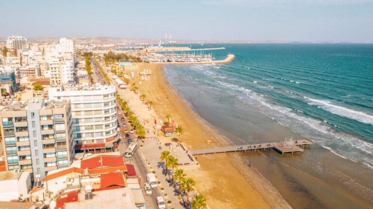 Plaża Finikoudes w Larnace z lotu ptaka, pomost, palmy i hotele wzdłuż nadmorskiej ulicy