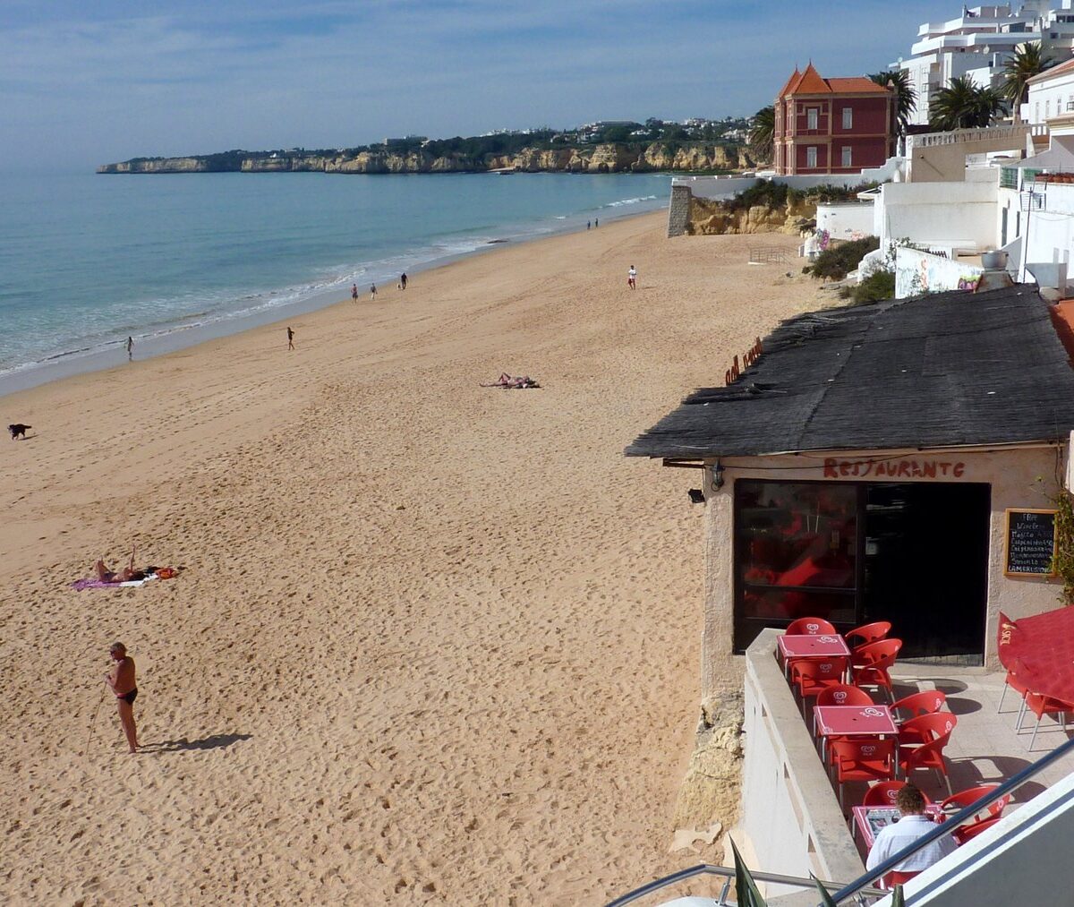 Plaża Armação de Pêra pod białymi domami i restauracją, w oddali klify nad morzem