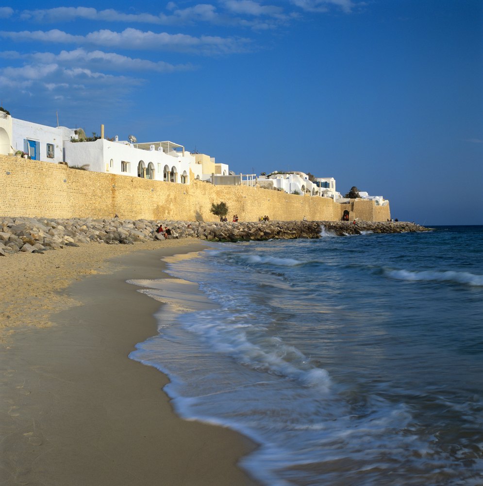Piaszczysta plaża pod kamiennymi murami medyny Hammametu, nad murami białe domy