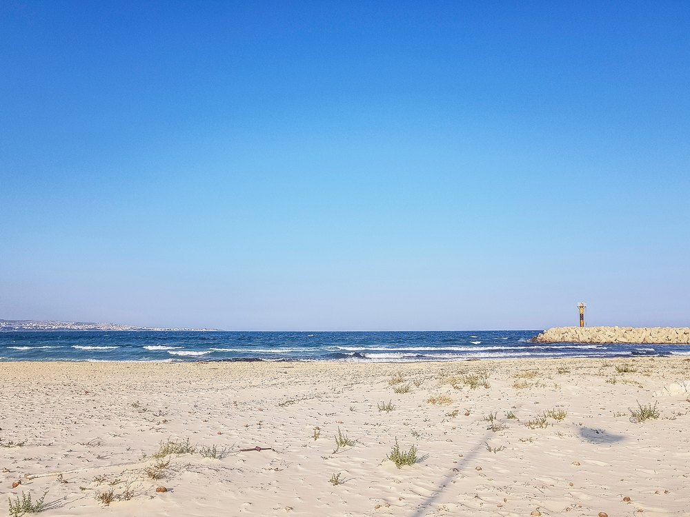 Pusta piaszczysta plaża przy marinie Yasmine Hammamet, w tle falochron z latarnią