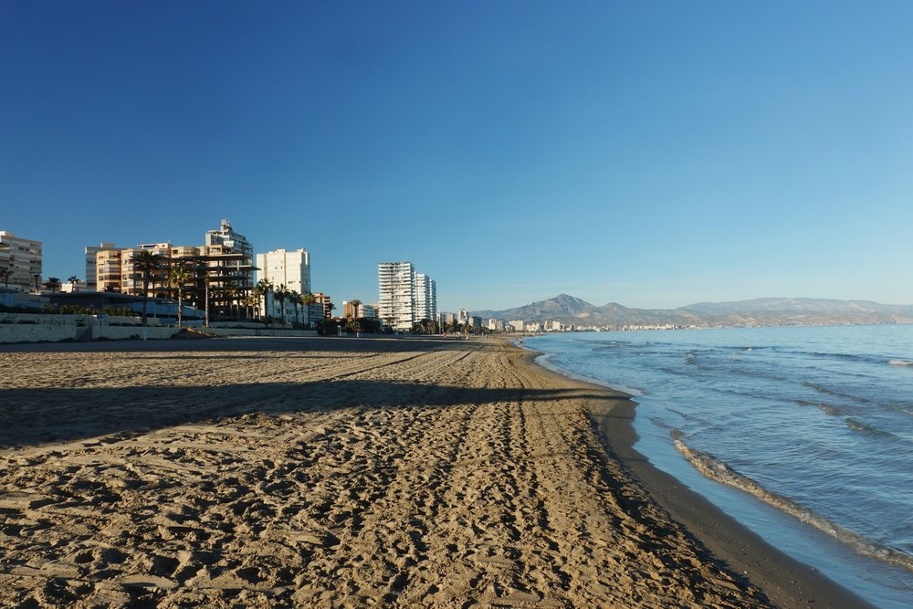 Szeroka plaża San Juan w Alicante o poranku, ślady na piasku i bloki wzdłuż brzegu
