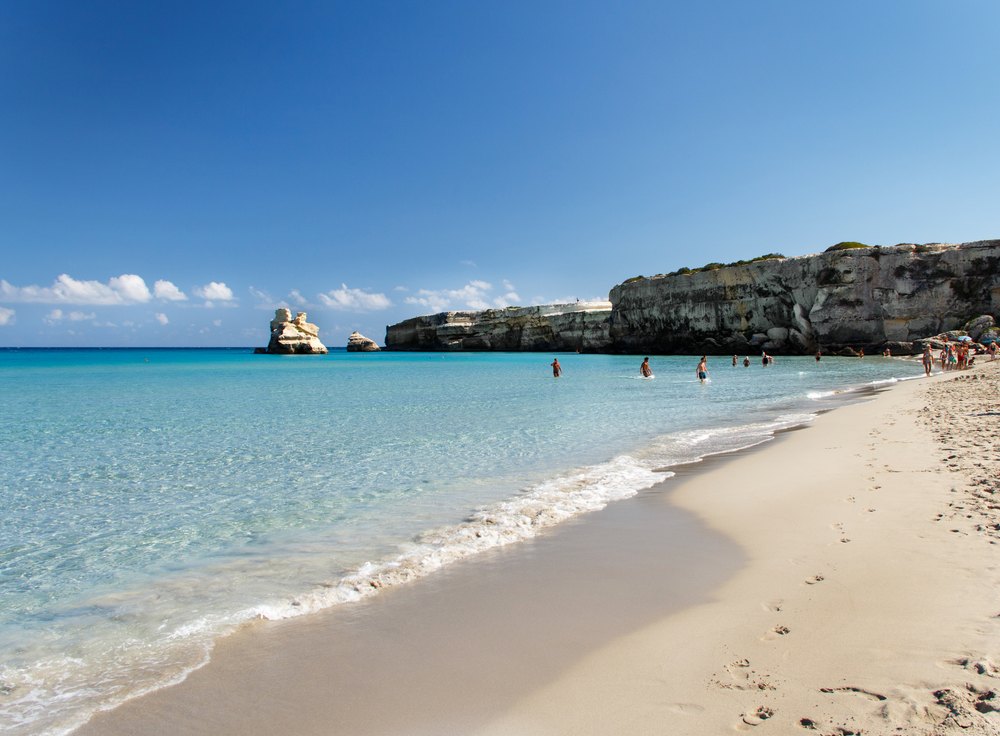Piaszczysta plaża Torre dell'Orso z turkusową wodą, w tle wapienne klify i dwie skały w morzu