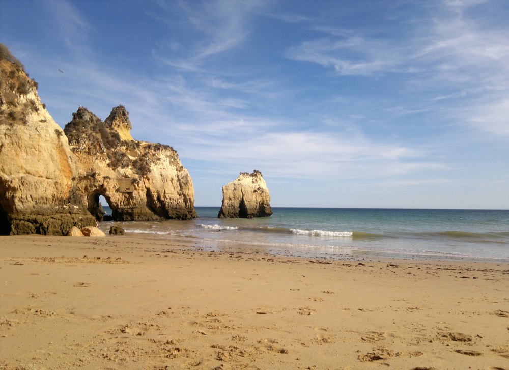 Praia dos Três Irmãos w Alvorze, piasek pod złotymi skałami z łukiem i skała w morzu