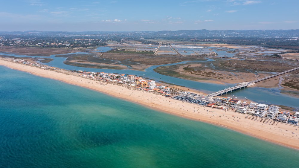 Praia de Faro na mierzei z domami wzdłuż plaży i mostem do lądu, za nią laguna
