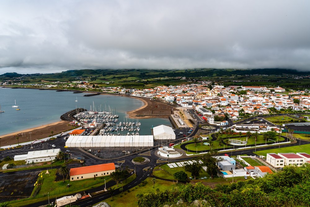 Praia da Vitória z góry: piaszczysta plaża miejska nad zatoką, marina i zabudowa miasta pod chmurami
