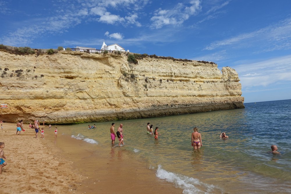 Praia Nova pod wysokim złotym klifem, na górze biała kaplica Nossa Senhora da Rocha
