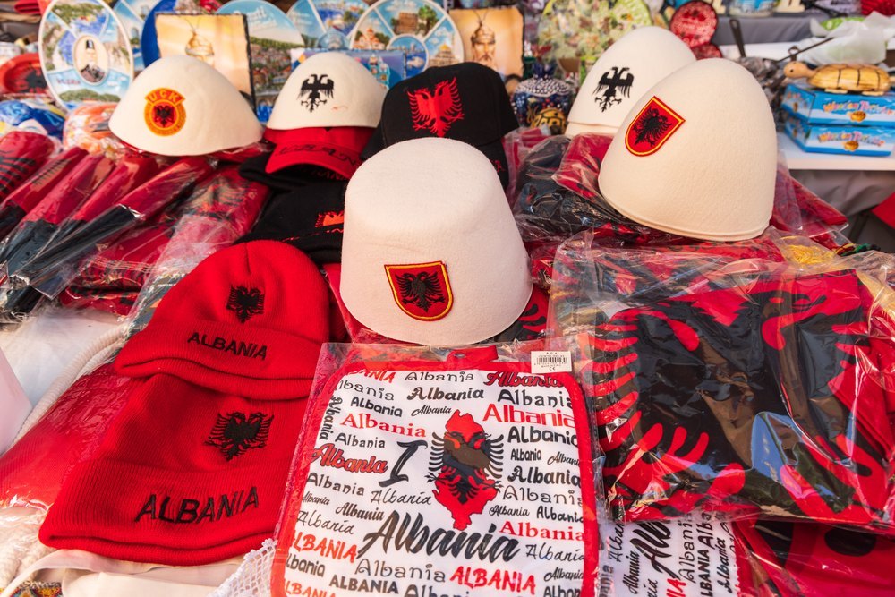 Białe filcowe czapki qeleshe z orłem i czerwone czapki z napisem Albania na straganie