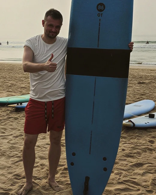 Rafał Nowak, autor SmartWakacje.pl, na plaży z deską surfingową