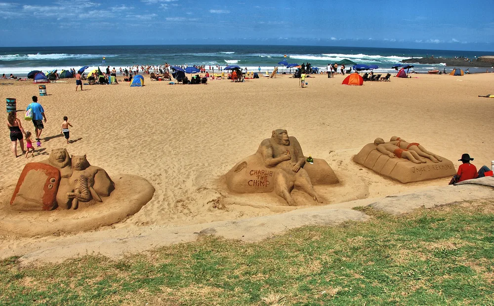 Rzeźby z piasku na plaży w Amanzimtoti, za nimi parasole plażowiczów