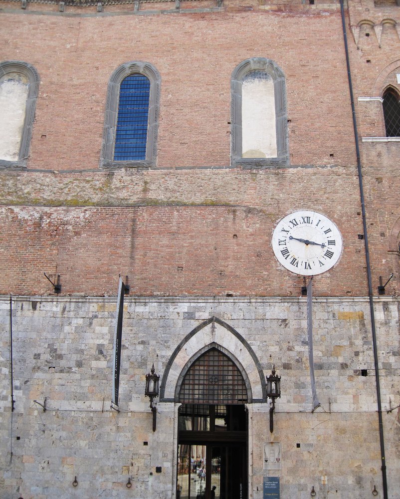 Ceglano-kamienna fasada Santa Maria della Scala z zegarem i gotyckim portalem naprzeciw katedry