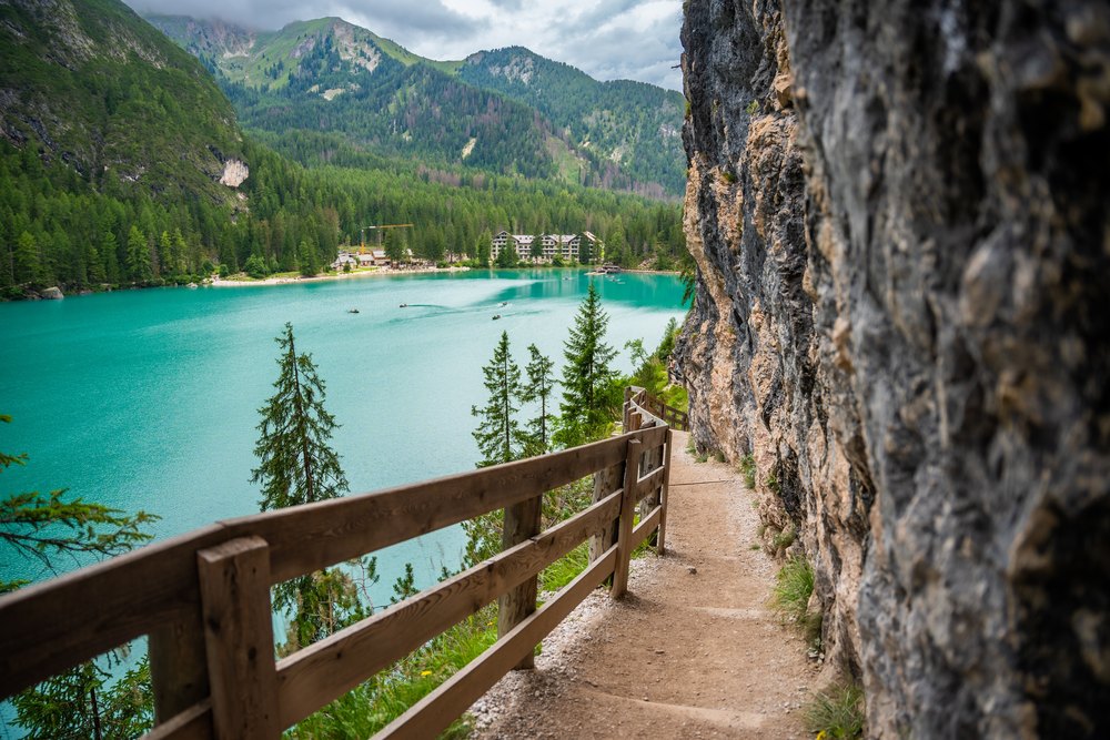 Ścieżka z drewnianą barierką wzdłuż skały nad turkusowym Lago di Braies