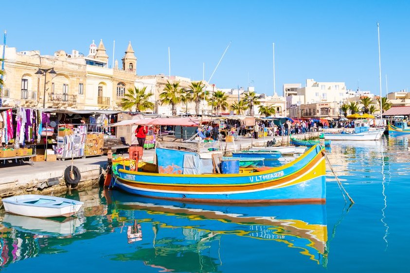 Stragany z pamiątkami i kolorowe łodzie luzzu w porcie Marsaxlokk