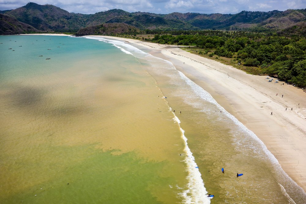 Surferzy na falach przy długiej plaży Selong Belanak na Lomboku, z lotu ptaka