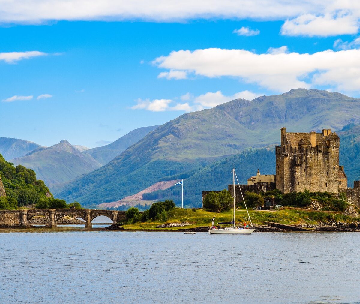 Zamek Eilean Donan na wysepce połączonej kamiennym mostem, za nim góry Highlands