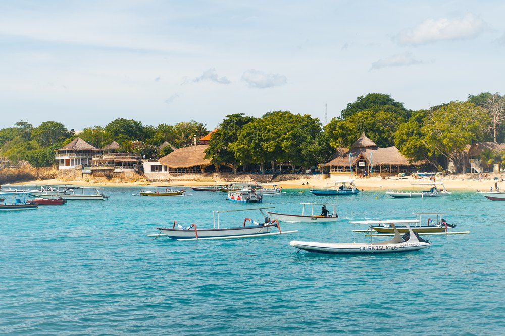 Łodzie na turkusowej wodzie zatoki Mushroom Bay przed plażą z hotelami na Nusa Lembongan