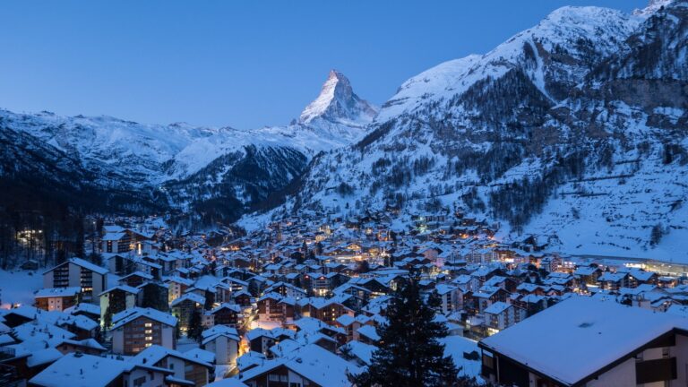 Zaśnieżona wieś Zermatt o zmierzchu, nad doliną szczyt Matterhornu